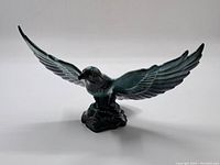 Front perspective angle of dark green glazed ceramic bird with spread wings on base, showing detailed wing feathers and bird facial features.