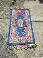 Full view of vintage British India style rug laid on stone pavement showing the entire rug including the fringed edges and central floral design.