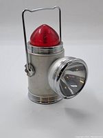 Front and angled views of the vintage Ford lantern showing metal body, chrome accents, side flashlight reflector, and red dome light on top with handle.