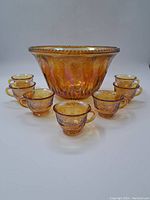 Front view of vintage amber glass punch bowl centered with seven matching cups arranged around it.