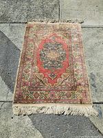 Full view of the vintage hand-knotted carpet laid on concrete, showing the central medallion and floral patterned border with fringe on one end.