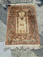 Full view of the vintage hand-knotted carpet laid on pavement, showing fringe and overall pattern.