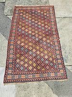 Full view of the vintage Persian carpet laid out on a concrete surface showing the geometric diamond pattern and colorful design.