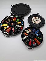 Opened view of two round plastic tire-shaped storage containers revealing multiple colorful vintage Hot Wheels toy cars inside slots.