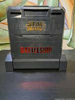 Closed case showing embossed Star Wars and Battleship logos on black plastic surface with handle.