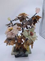 Front angle showing pastel carved flowers and brown leaves on stone base.