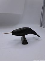 Left side view of the carved stone narwhal sculpture showing the mounted stone base and spiral tusk.