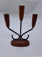 Full view showing the teak base, black metal arms, and three wooden candle cups with brass tops.