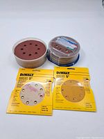 All sanding discs displayed with original DeWalt packaging and additional loose discs in plastic containers.