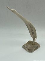 Side angle view of carved stone bird standing on base, showing elongated neck and beak