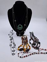 Full lot of five assorted vintage necklaces displayed on black stand and laid out flat.