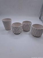 Four small white ceramic planters with textured surface designs displayed in a row on a plain background
