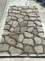 Full view of the entire rectangular rug laid flat outdoors showing the stone pattern and colors.