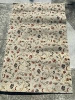 Full view of the cream background rug with floral vine pattern laid flat on stone surface.