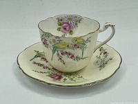 Tea cup and saucer set showing floral and yellow bird design with gold trim on scalloped edges and cup handle.