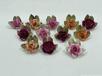 All 12 porcelain guess card stands shaped like roses in pink, peach, and burgundy with green leaves, arranged in rows.