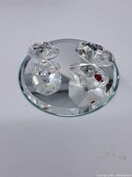 Two Swarovski crystal clam figures displayed on a round mirrored base, showing clear faceted crystal and red heart detail.