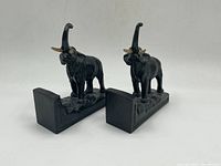 Pair of vintage cast metal elephant bookends photographed from an angle showing raised trunks and detailed sculpting on a plain background.