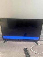 32 inch Toshiba TV displayed face front on carpet with remote control in front. TV screen shows a blue bar at the bottom with no active image.