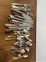 Top view of assorted silver plated forks, knives, and spoons laid out on a wooden surface.
