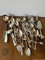 Mixed silver-plated spoons, forks, ladles, tongs, and servers on wooden surface