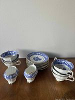 All pieces arranged on wooden surface, showing teacups, saucers and creamers with pattern details