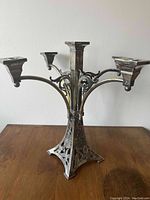 Metal candelabra showing four arms with square candle holders and ornate pierced base on wooden surface