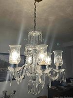 Photo showing the glass crystal chandelier lit with multiple bulbs and hanging crystal prisms, suspended from a chain.