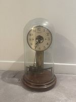 Front view of brass anniversary clock with glass dome showing dial and torsion pendulum