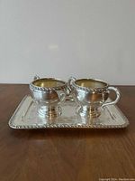 Photo showing the silver plated cream and sugar set on a silver plated rectangular tray with detailed rim.