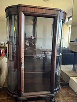 Photo of a large wooden curio cabinet with glass front and curved glass sides, empty interior with multiple shelves visible.