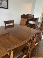 Wide angle showing wooden dining table and several matching chairs with cushioned seats.