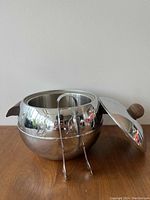 Polished stainless steel ice bucket with lid and ice tongs on wooden surface