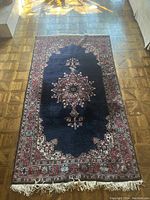 Full view of rug laid flat on parquet floor showing central medallion, border and fringe.