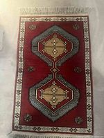 Photo of the full Kerman area rug laid flat showing the geometric medallion design in red, beige, and blue with fringe on short ends.