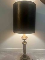 Front view of lamp illuminated, showing cylindrical black shade and detailed metal base.