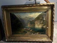 Overall view of painting depicting mountain lake scene with cows, ornate gilt frame and top-mounted light fixture