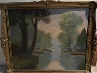 Image of an oil landscape painting showing a river running through trees and greenery with an ornate gold frame.