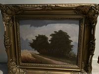 Framed oil painting showing rural landscape scene with trees, path, grass, and cloudy sky. Signed by Joyce Duffy.
