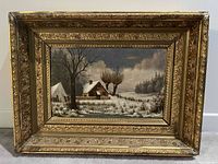 Framed winter landscape oil painting showing snow-covered countryside cabin, trees, fence, and cloudy sky with ornate gold frame measuring approximately 23x18 inches.