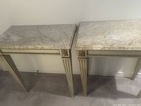Frontal shot showing both marble top tables, painted wood frames, tapered fluted legs and carved detailing