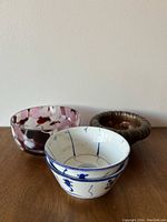 Photo of three decorative bowls: a blue and white patterned ceramic bowl, a marbled pink and white glass bowl, and a brown fluted ceramic bowl on a wooden surface.
