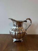 Single silver water pitcher on a wooden surface against a plain wall background.