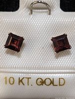Closeup image showing two square-cut garnet stud earrings mounted on a white card labeled 10 KT GOLD.