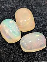 Three genuine opal cabochons displayed on a black cloth, showing play of color and smooth polished surfaces.