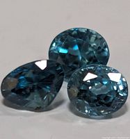 Close-up photo showing three blue zircon gemstones on a neutral background highlighting their facets and deep blue color.