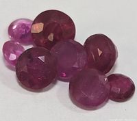 Close-up image showing faceted genuine ruby gemstones in various sizes, red to pinkish hues, with visible inclusions.