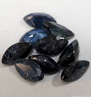 Seven loose marquise cut sapphire gemstones with visible surface inclusions, deep blue color
