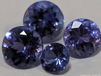 Close-up photo of four round faceted tanzanite gemstones showing vivid violet-blue color and clarity.