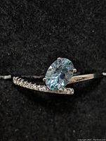 Close-up photo of the sterling silver ring with oval blue topaz and small clear stones on band, displayed on black fabric.